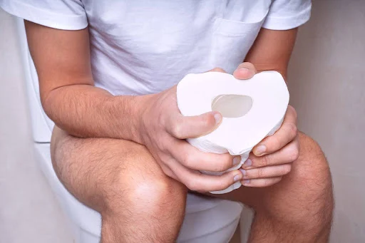 A person sitting on toilet with tissue paper roll in hands